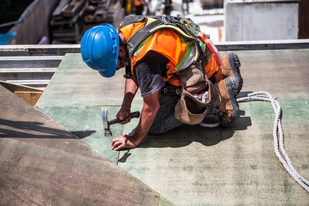 construction worker on a roof pounding a nail